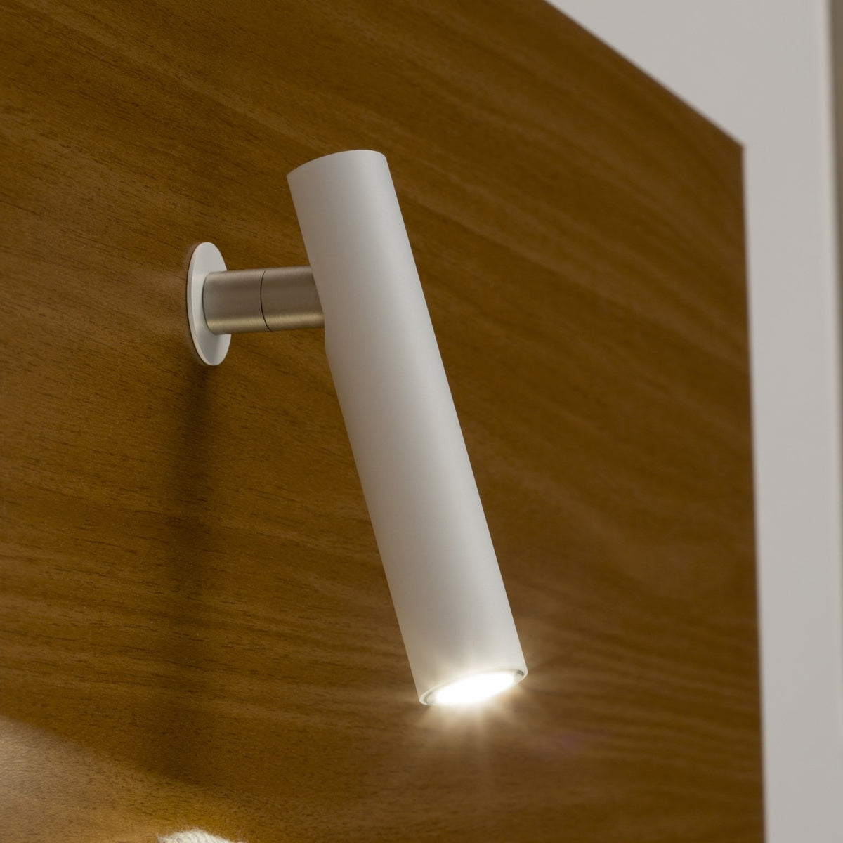 Ivelline LED wall light with reading light in white, slim cylindrical head angled downward on a short silver arm with round wall rosette, mounted on wood panelling.