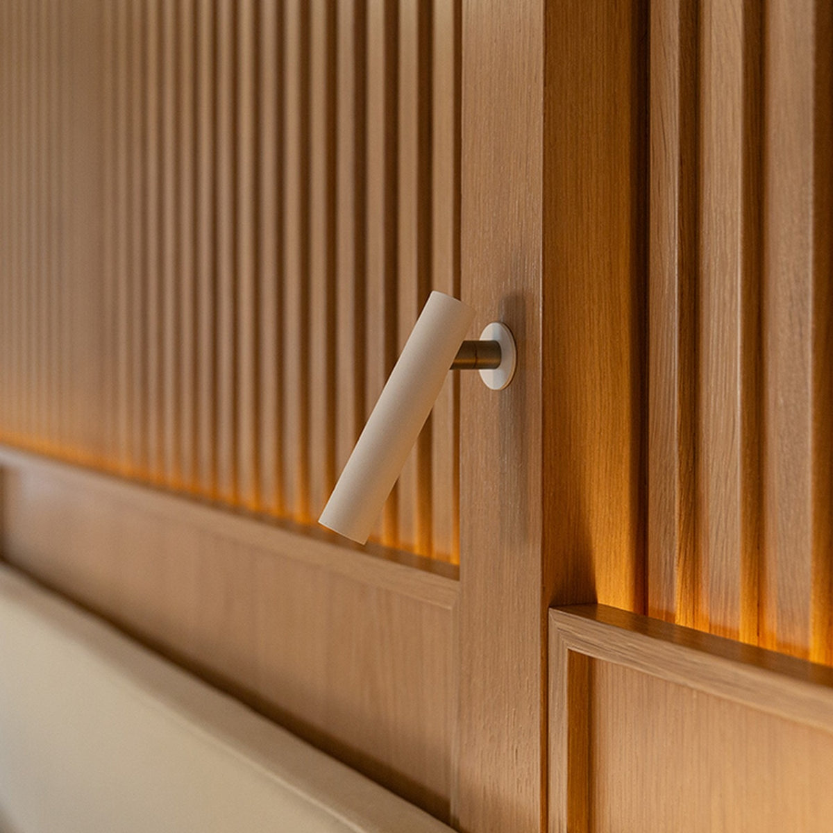 Ivelline LED wall light with reading light in white, cylindrical head on short arm with round rosette, mounted on fluted wood panelling.