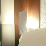 Flat Wall Light with Reading Light in white, a slim rectangular iron plate mounted above a bed, casting a warm indirect glow with a slender integrated LED reading arm beneath it.