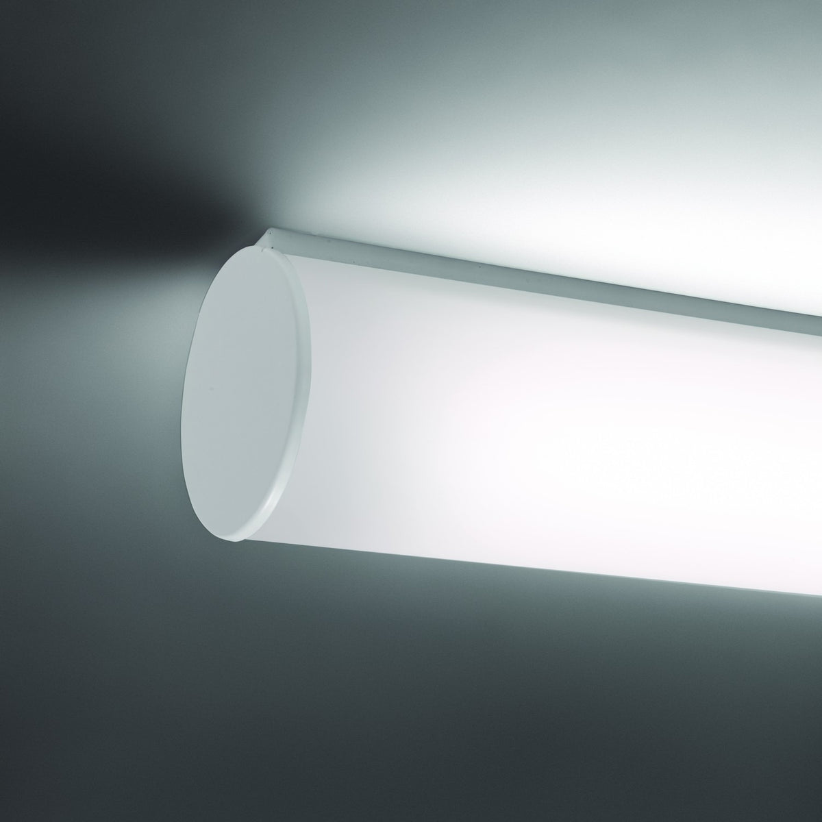 Bath A LED Linear Flush Wall & Ceiling Light in white, showing an illuminated opal polycarbonate tube with a round white end cap, mounted near a ceiling corner.