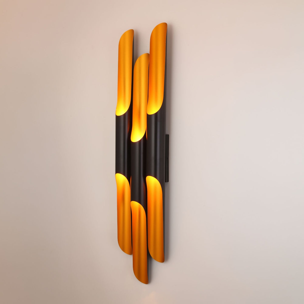 Niori Stealth 6 Light wall light with staggered matt black cylindrical tubes and brushed brass interiors, mounted vertically on a neutral wall.