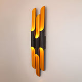 Niori Stealth 6 Light wall light with staggered matt black cylindrical tubes and brushed brass interiors, mounted vertically on a neutral wall.