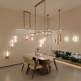 Elvaris LED Small Vertical Alabaster Wall Light in brushed brass, shown illuminated on a dining room wall with warm white glow through the stone column.