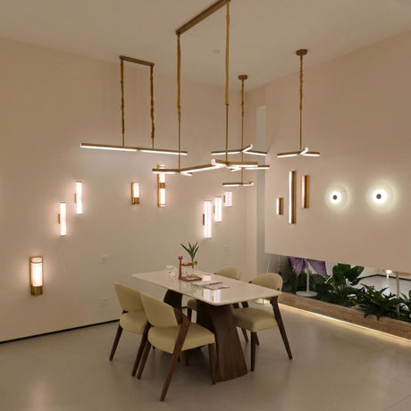 Elvaris LED Small Vertical Alabaster Wall Light in brushed brass, shown illuminated on a dining room wall with warm white glow through the stone column.
