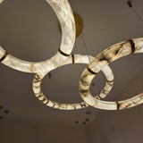 Aureon LED Triple Ring Alabaster Chandelier in brushed brass, close-up view of overlapping alabaster hoops with brass banding suspended from a ceiling canopy.