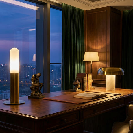 A sophisticated office features a large wooden desk, modern lamps, green curtains, books, a sculpture, and a dusk cityscape. The Altessa 1 Light Large Vertical Alabaster Table Lamp in Soft White & Brass warmly lights the open book on the desk.
