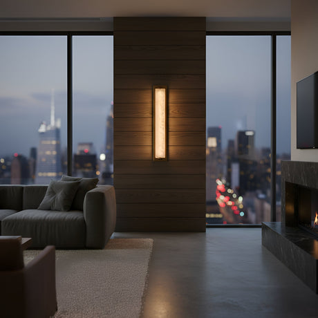 A modern living room with the Valora LED Vertical Panel Alabaster Wall Light in soft white and brushed brass, large windows overlooking a cityscape at dusk, a gray sofa, fireplace, and gentle ambient lighting.