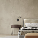MiniSpot LED Wall Light in black iron above a bedside table, featuring a round base plate and angled rod with cylindrical spot head, shown mounted in a bedroom setting.