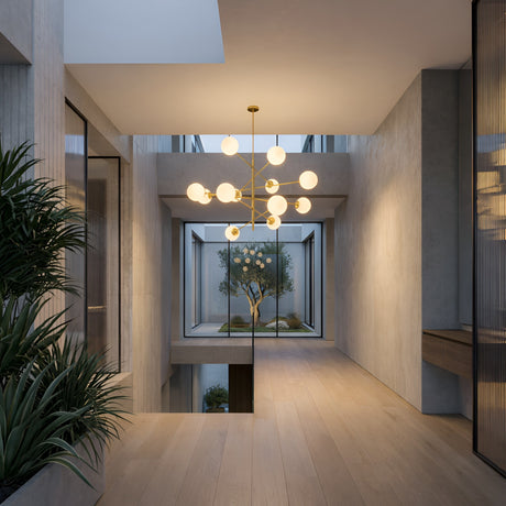 A modern hallway with light wood floors, large windows, and indoor plants features a minimalist, airy design. A glass wall reveals an inner courtyard with an olive tree. The space is highlighted by the striking Tortora 10 Light Suspension - Gold.