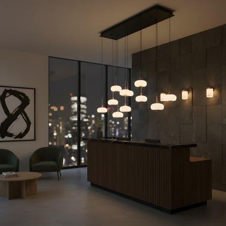 Niori Aurevia 14 Light LED linear chandelier in matt black and brass with staggered alabaster domes above a wood reception desk by a city-view window.