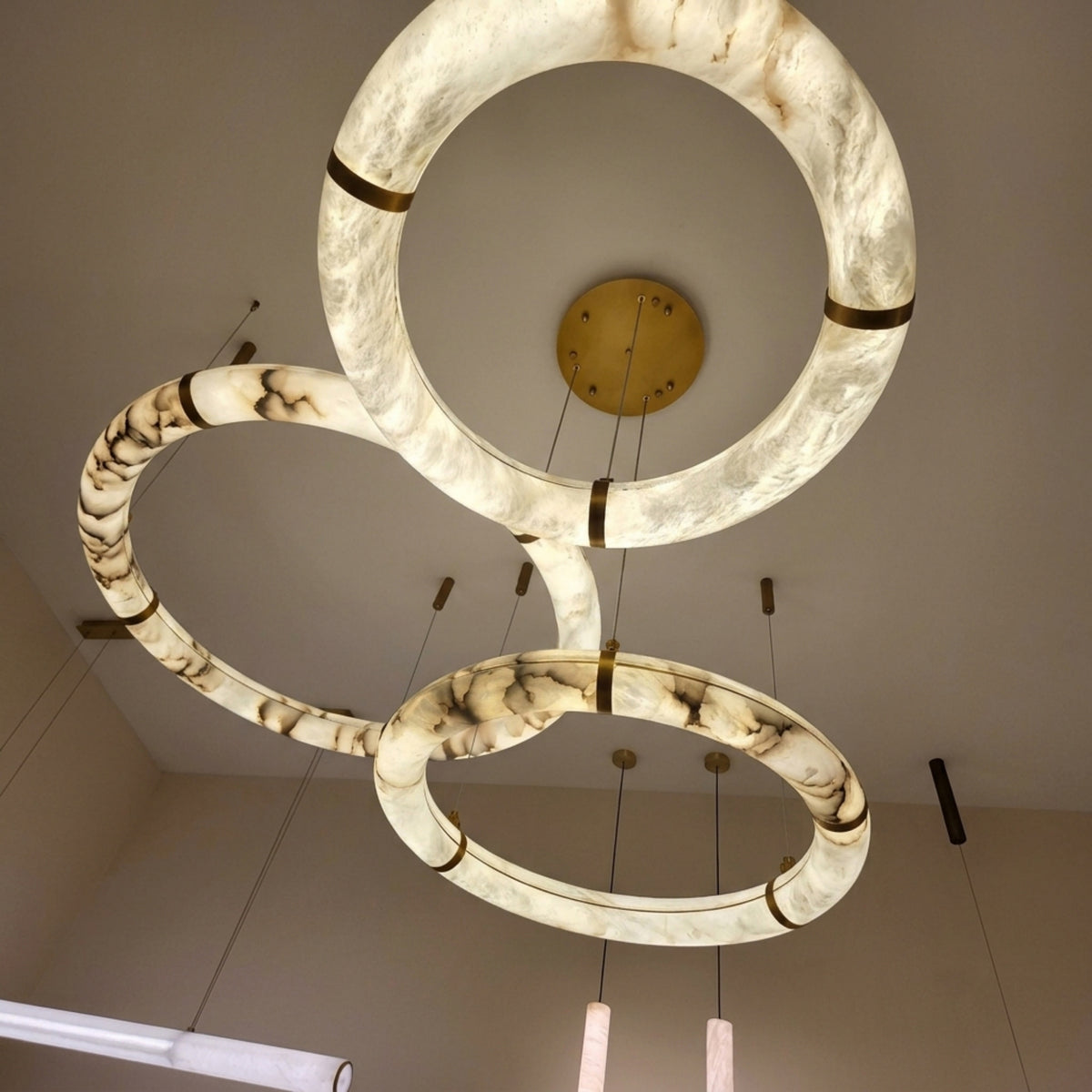 Aureon LED Triple Ring Alabaster Chandelier in brushed brass, three interlocking marbled alabaster hoops with brass accents, viewed from below against a plain ceiling.