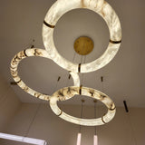 Aureon LED Triple Ring Alabaster Chandelier in brushed brass, three interlocking marbled alabaster hoops with brass accents, viewed from below against a plain ceiling.