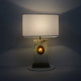 Selune alabaster table lamp lit at night, showing rectangular fabric shade, brushed brass stem and plinth, and glowing agate slice inset.