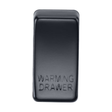 A close-up of a rectangular switch cover labeled "Marked WARMING DRAWER" in matte black. The interchangeable cover features a smooth, glossy finish with slightly rounded edges.