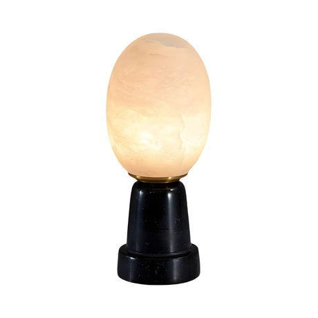 The Ovolis 1 Light Oval Alabaster Table Lamp in soft white and black features a sculptural design with natural Spanish stone, a warm glow, and sits on a smooth black cylindrical base against a plain white background.