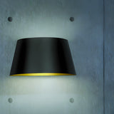 Fennorne Wall Light in black with a tapered iron shade and gold interior, mounted on a grey textured wall, casting a soft downward glow.