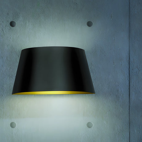 Fennorne Wall Light in black with a tapered iron shade and gold interior, mounted on a grey textured wall, casting a soft downward glow.