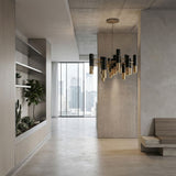 Modern minimalist interior with concrete walls, large windows overlooking the city, built-in shelving with green plants, and the Leonard 19 Light LED Chandelier in black and gold as a striking centerpiece.