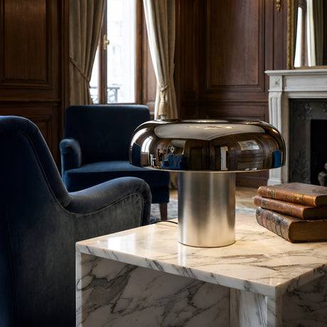 The Arven LED Mushroom Form Marble Table Lamp in soft white and black sits on a marble side table with stacked books, surrounded by blue armchairs and curtained windows in a classic wood-paneled living room.