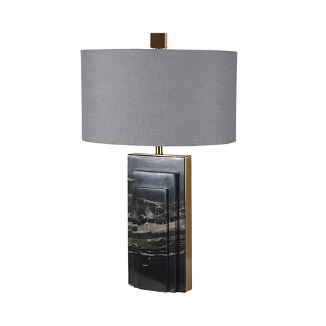 The Caldrin 1 Light Marble Table Lamp - Brass & Black features a modern rectangular black and gray marble base with brass accents and a large cylindrical gray fabric shade, beautifully set against a white background.