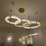 Aureon LED Triple Ring Alabaster Chandelier in brushed brass, three staggered glowing rings suspended from a round ceiling canopy in a warm-toned living space.