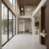 Minimalist, modern interior with tall ceilings, large glass doors, a Tree 8 Light Suspension - Gold as the contemporary chandelier, indoor plants, a built-in bench, and neutral walls and floors. Natural light fills the spacious hallway.