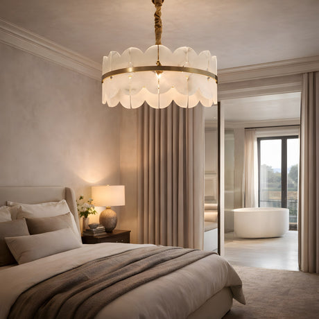 A serene, modern bedroom in neutral tones features the Petraia LED 1 Tier Floral Alabaster Chandelier in Brushed Brass & Soft White, a plush bed with layered bedding, a nightstand with lamp and vase, tall curtains, and a view of a freestanding bathroom tub.