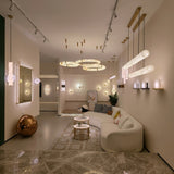 Aureon LED Triple Ring Alabaster Chandelier in brushed brass, three staggered circular hoops suspended above a living room seating area with warm ambient light.