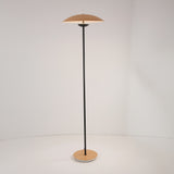 The Ex-Display Ginger LED Floor Lamp in Black & Oak features a thin pole, round oak base, and a shallow dome shade, embodying minimalist style and modern elegance against a plain white background.
