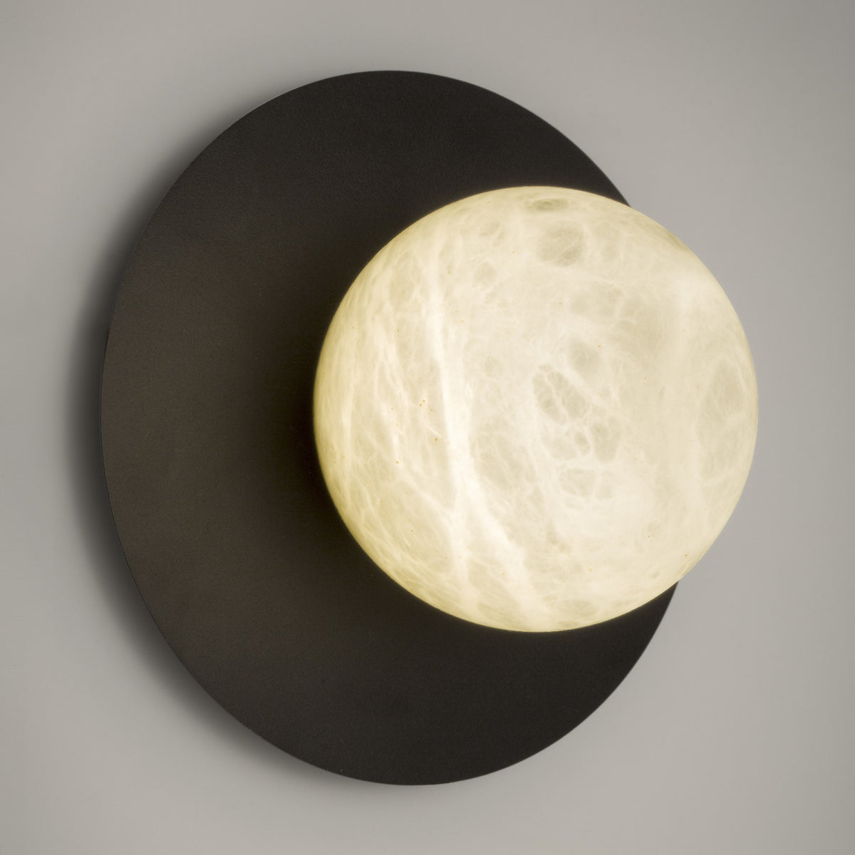 Halvessa LED Alabaster Dimmable Wall Light in Black, a round black iron disc with an off-centre alabaster globe showing soft cloudy veining, on a plain grey background.