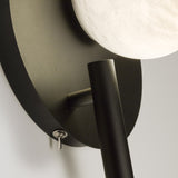 Close-up of the Halvessa LED wall light showing the black iron backplate, toggle switch, angled reading arm, and glowing alabaster globe.
