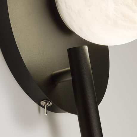 Close-up of the Halvessa LED wall light showing the black iron backplate, toggle switch, angled reading arm, and glowing alabaster globe.