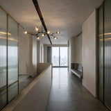 Niori Tree 7 Light Suspension in black with seven glass globes on branching arms, illuminating a minimalist hallway with frosted glass walls and city view.