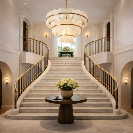 Grand foyer with a double curved staircase, a round table topped with white flowers, and the Petraia LED 3 Tier Floral Alabaster Chandelier in Brushed Brass & Soft White overhead, with natural light streaming through the window.