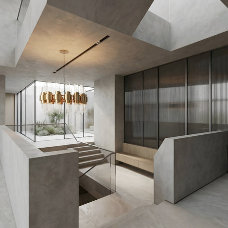 A modern interior with concrete walls, a glass-railed staircase, the Tycho 6 Light Crystal Chandelier in gold & white, built-in bench seating, and floor-to-ceiling windows overlooking a minimalist courtyard garden.