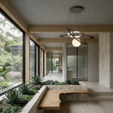 A modern hallway with large windows, indoor succulents in a stone planter, a wooden bench, minimalist décor, and the Universe LED Suspension Light in bronze, all overlooking lush greenery outside.