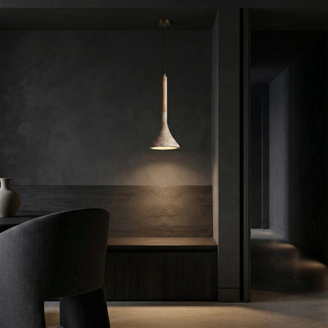 A modern, minimalistic interior with dark walls and furniture features the Vantoro 1 Light Cone Travertine Single Pendant Light in light brown and beige, casting a warm glow over a wooden bench and table. A ceramic vase and curved chair are partially visible.