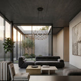 A modern living room with minimalist gray sofas, a square coffee table, large windows overlooking a courtyard with trees, neutral-toned decor, abstract wall art, and the striking Mesh LED Medium Suspension Light - Black as the sculptural chandelier.