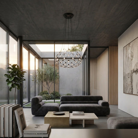 A modern living room with minimalist gray sofas, a square coffee table, large windows overlooking a courtyard with trees, neutral-toned decor, abstract wall art, and the striking Mesh LED Medium Suspension Light - Black as the sculptural chandelier.