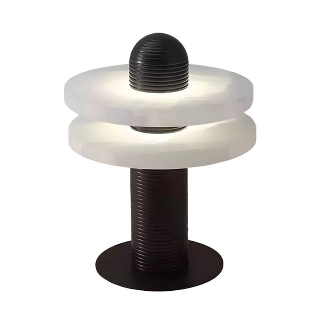 The Nyxara LED Double Tiered Alabaster Table Lamp features a cylindrical black base, two frosted white rings separated by a gap, and a grooved black column. Lit in soft white and black, it creates a modern, glowing ambiance.