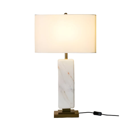 The Caldris 1 Light Solid Marble Table Lamp features a rectangular white marble base, brass accents, and a large cylindrical white shade with a black cord and switch, shown on a plain white background.