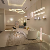 Aureon LED Triple Ring Alabaster Chandelier in brushed brass, three staggered circular rings suspended above a living room sofa, warm white ambient glow.