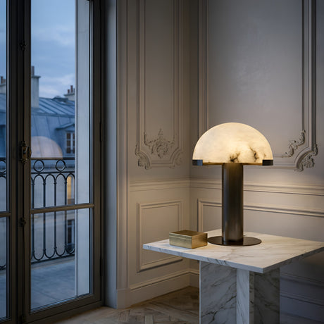 The Noctelis 1 Light Dome Alabaster Table Lamp in soft white & black sits on a white marble table in an elegant room with ornate walls, large windows, and a dusk city rooftop view.