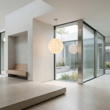 A modern minimalist interior with light stone floors, a built-in wooden bench, large glass walls, and a Lunar Pendant Light - White. The space opens to a courtyard featuring greenery and sleek architectural lines.