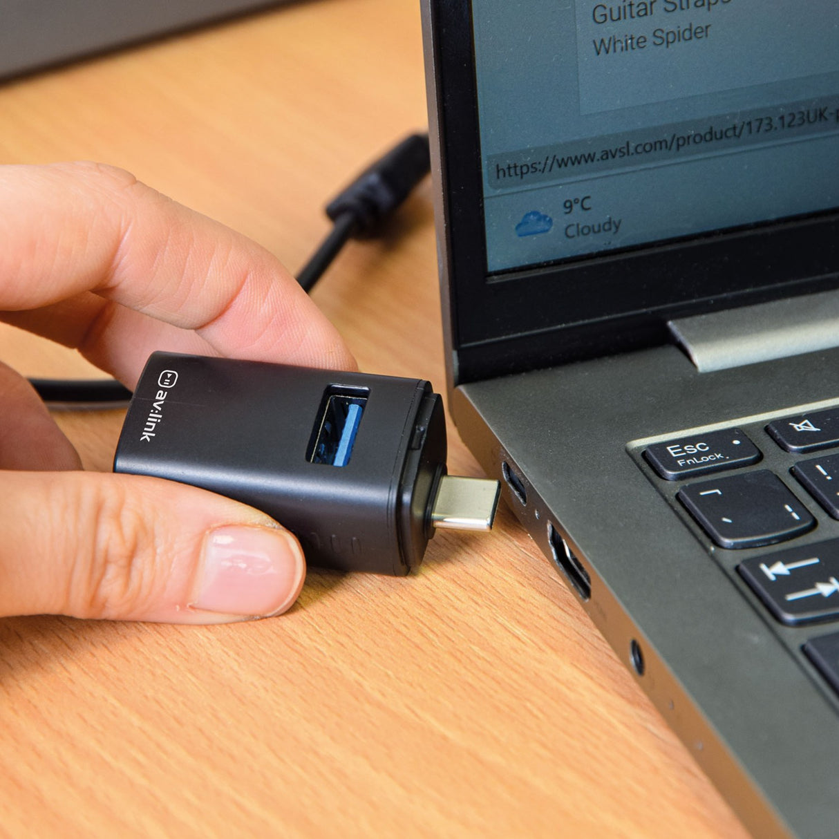 Hand plugging the AV:Link 3 Port Mini USB-C Hub in matt black into a laptop's USB-C port on a wooden desk, showing the USB-A ports.