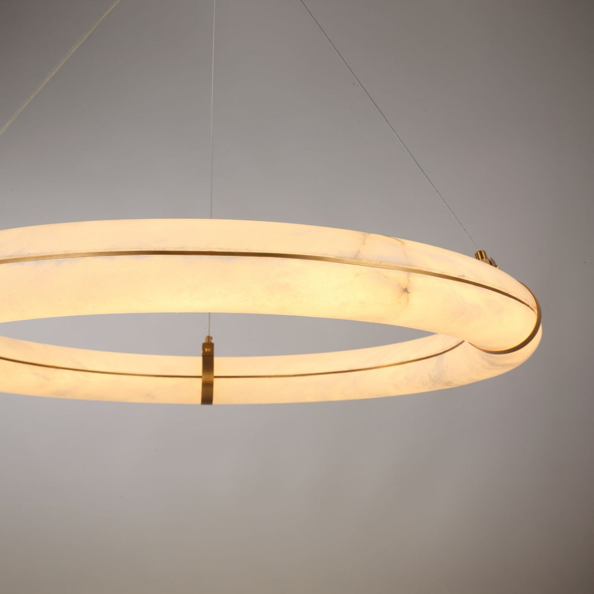 Aureon LED Alabaster Ring Chandelier 800mm, close-up of the glowing alabaster ring in brushed brass cradles with steel suspension cables, plain grey background.