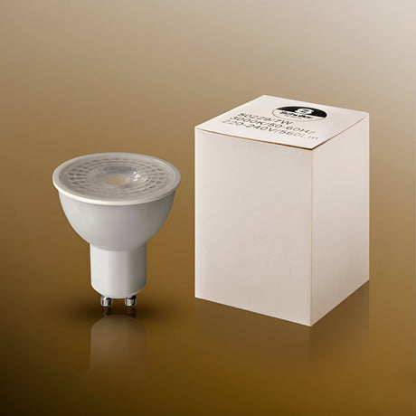 Schuller dimmable 7W GU10 LED spotlight bulb in white with clear lens, shown beside its printed cube packaging on a gold background.