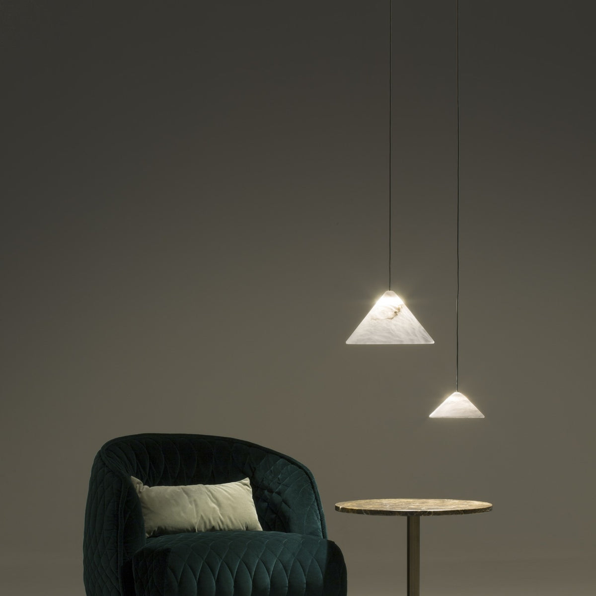Two Fuji pendant lights with cone-shaped alabaster shades and black flex cords hang above a dark green armchair and marble side table in a living room setting.