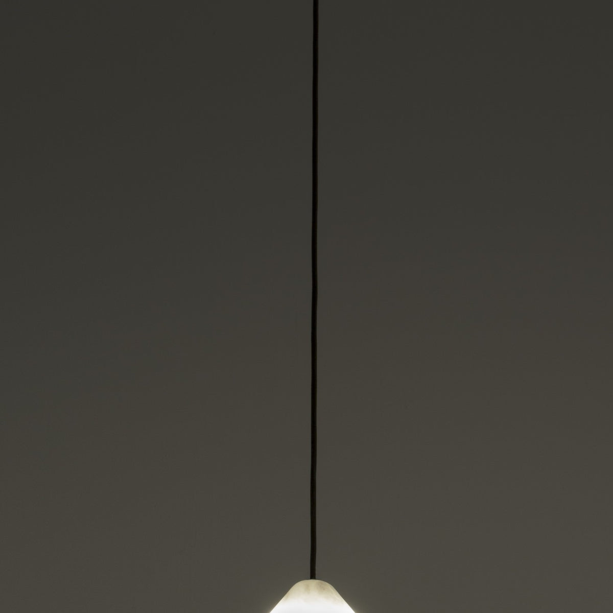 Fuji LED Alabaster Pendant Light with polished brass canopy and slim black cord, cone-shaped stone shade glowing warm white against a dark background.