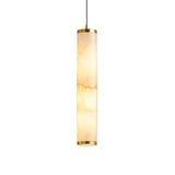 The Oria LED Medium Alabaster Single Pendant Light features a cylindrical soft white alabaster shade with brushed brass accents and is suspended by a thin black cord, creating a warm glow against a white background.